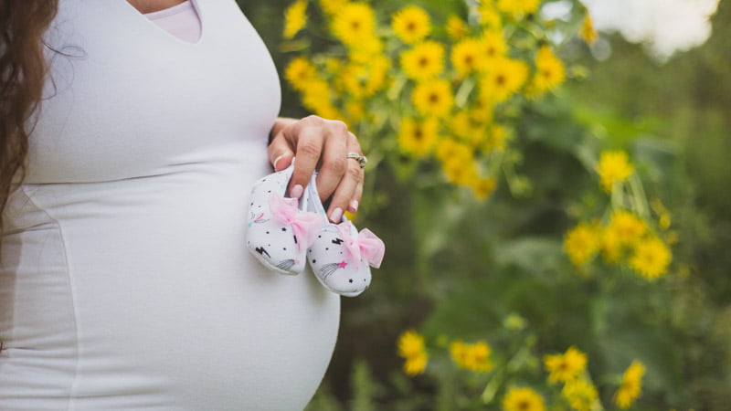A pregnant woman holding a pair of tiny shoes keeping them close to her belly