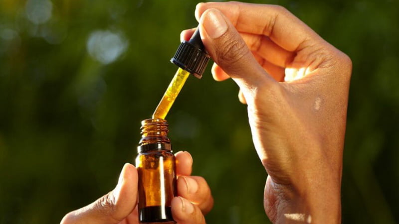 A person taking CBD oil out of a bottle from a glass dropper