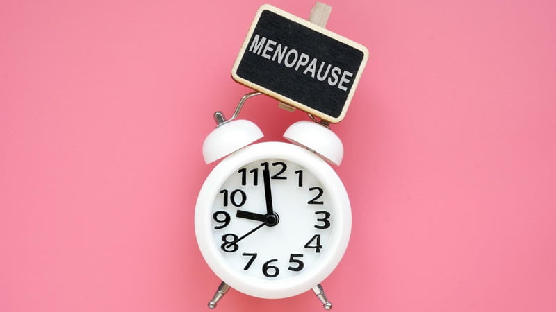 A white clock with a sign on top that reads "menopause" in pink background