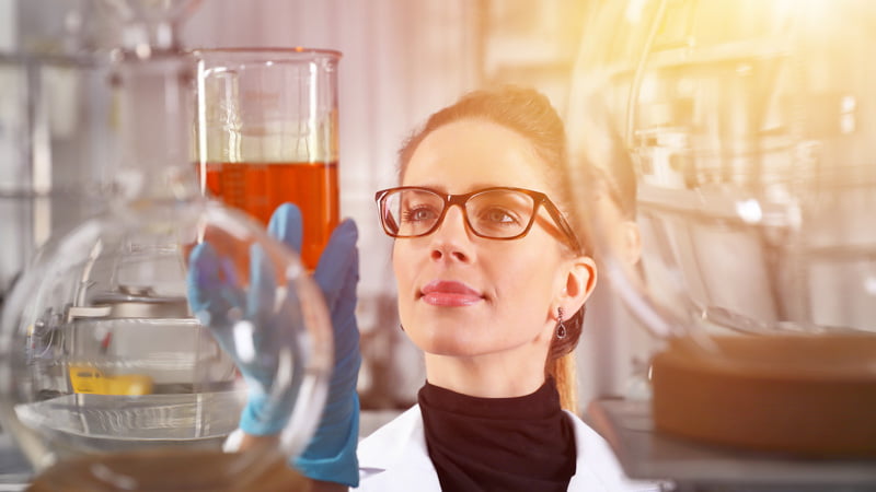 A woman scientist looking at a glass beaker full of hemp oil in a lab