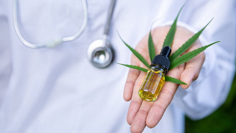 CBD oil and hemp leaf in a palm with a background of a doctor with a stethoscope