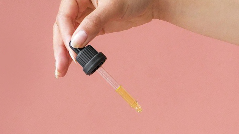 a women holding a cbd oil dropper on a pink background