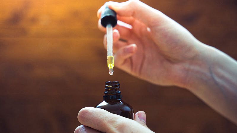CBD oil held by two hands in a brown background