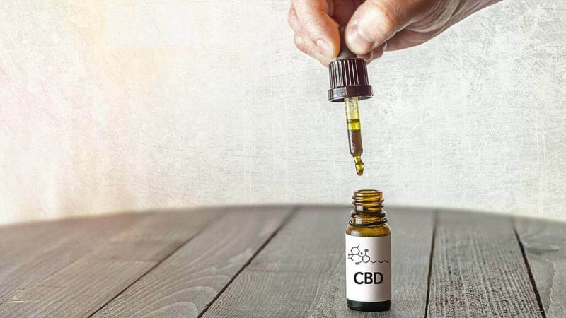 Hand Holding CBD Oil Pipette with Bottle in the Wood
