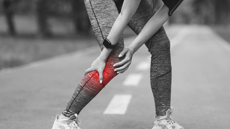 woman inn jogging outfit holds her right leg due to muscle spasm while on the road