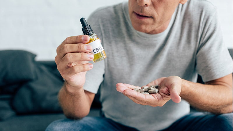 Man Sitting on Couch Holding CBD Oil and the other hand capsules