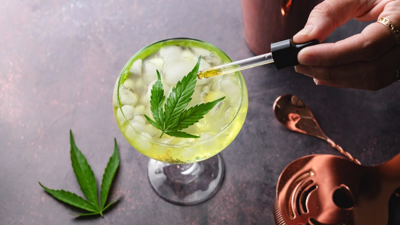 Hand Dropping CBD Oil on an Alcoholic Drinks with Hemp Leaf